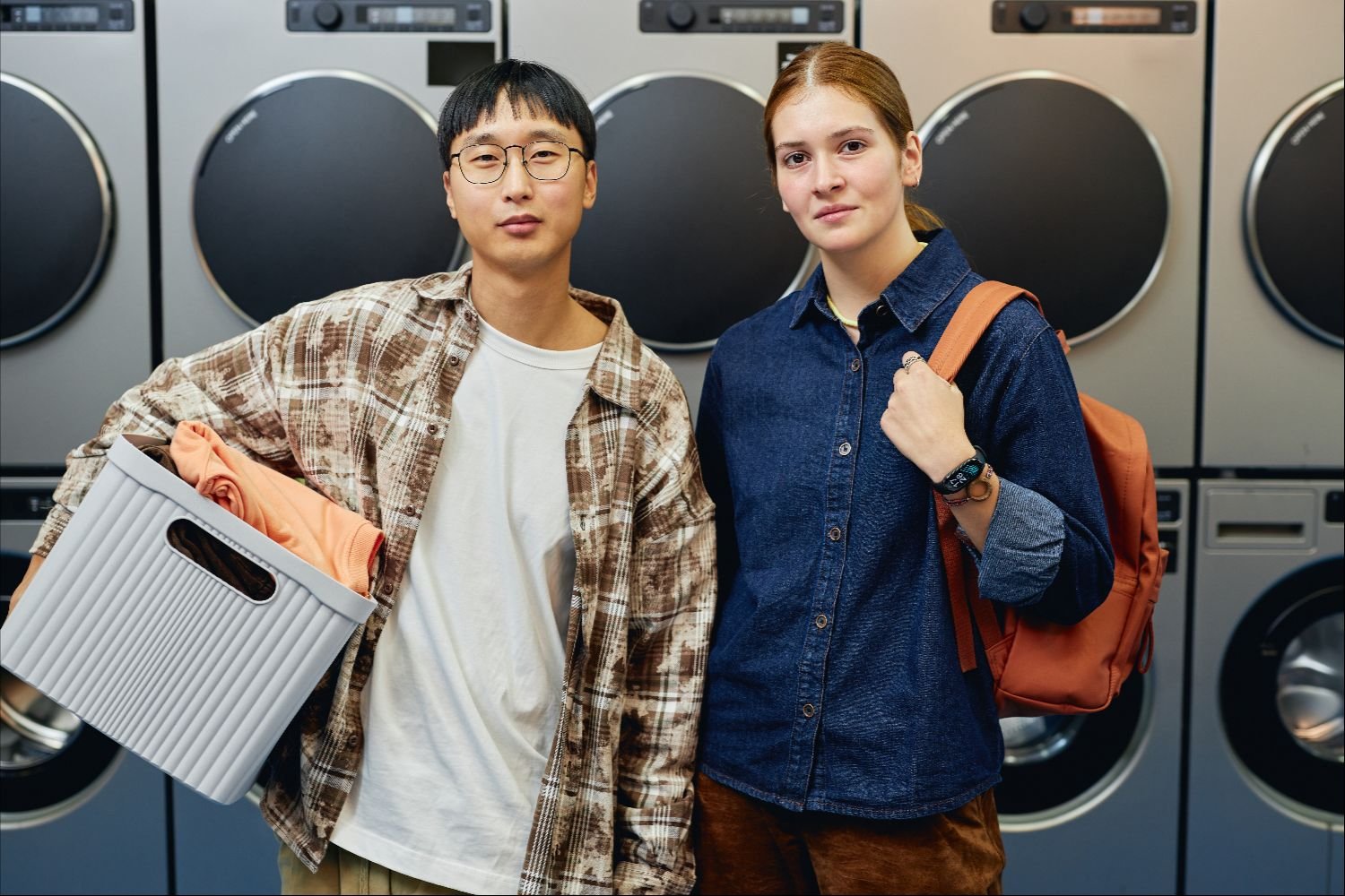 Young adults using a modern self-service laundromat with laundry basket